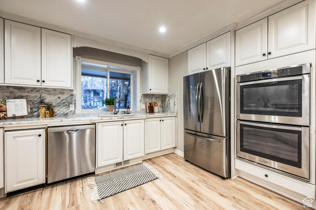 Kitchen featuring white cabinets, light hardwood / wood-style flooring, stainless steel appliances, and backsplash