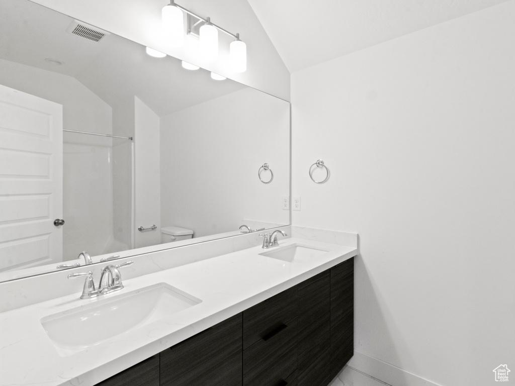Bathroom with toilet, dual vanity, and lofted ceiling