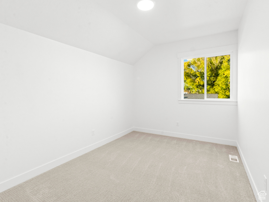 Spare room featuring light carpet and vaulted ceiling