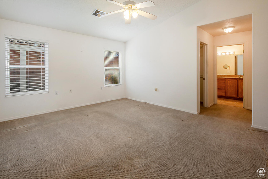 Unfurnished bedroom featuring ceiling fan, light colored carpet, and ensuite bathroom