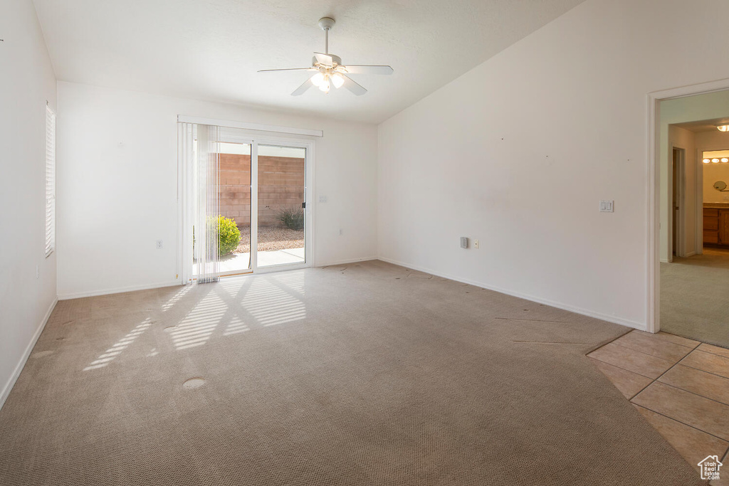 Empty room featuring light tile flooring, vaulted ceiling, and ceiling fan