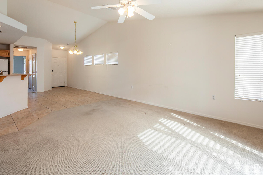 Unfurnished room featuring ceiling fan with notable chandelier, lofted ceiling, light tile floors, and a healthy amount of sunlight