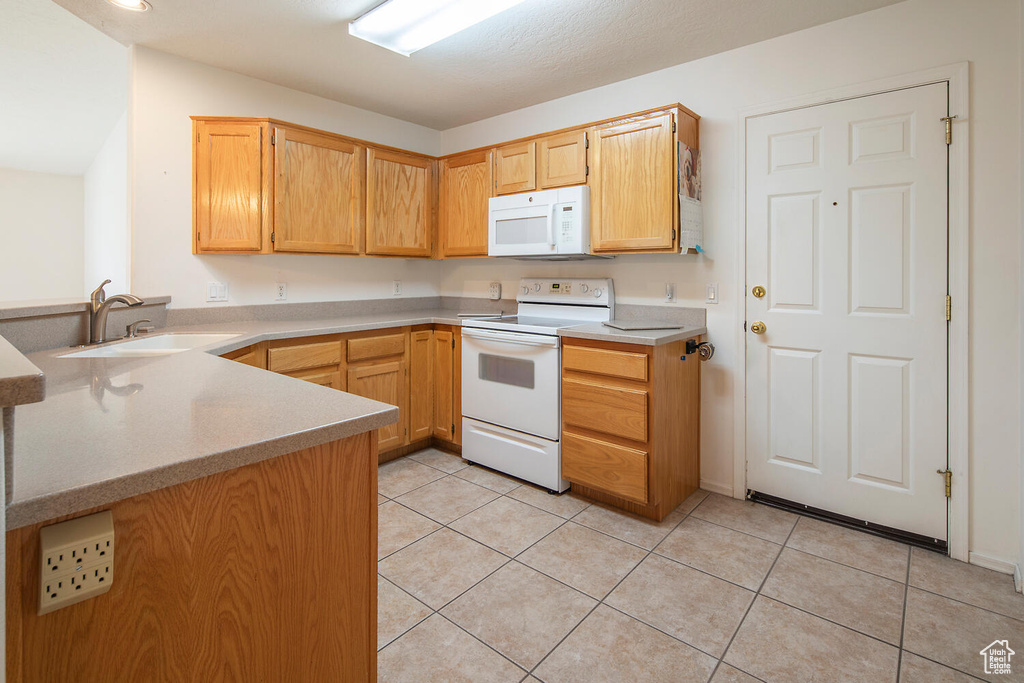 Kitchen featuring white appliances, sink, light tile flooring, and kitchen peninsula