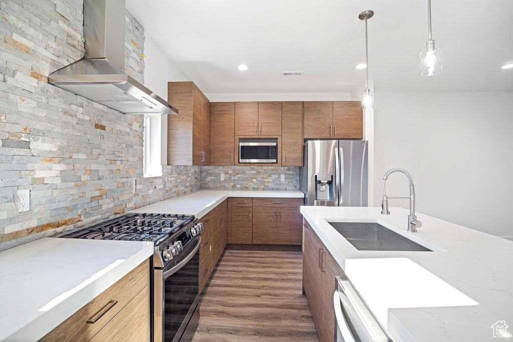Kitchen featuring dark wood-type flooring, tasteful backsplash, sink, stainless steel appliances, and wall chimney range hood