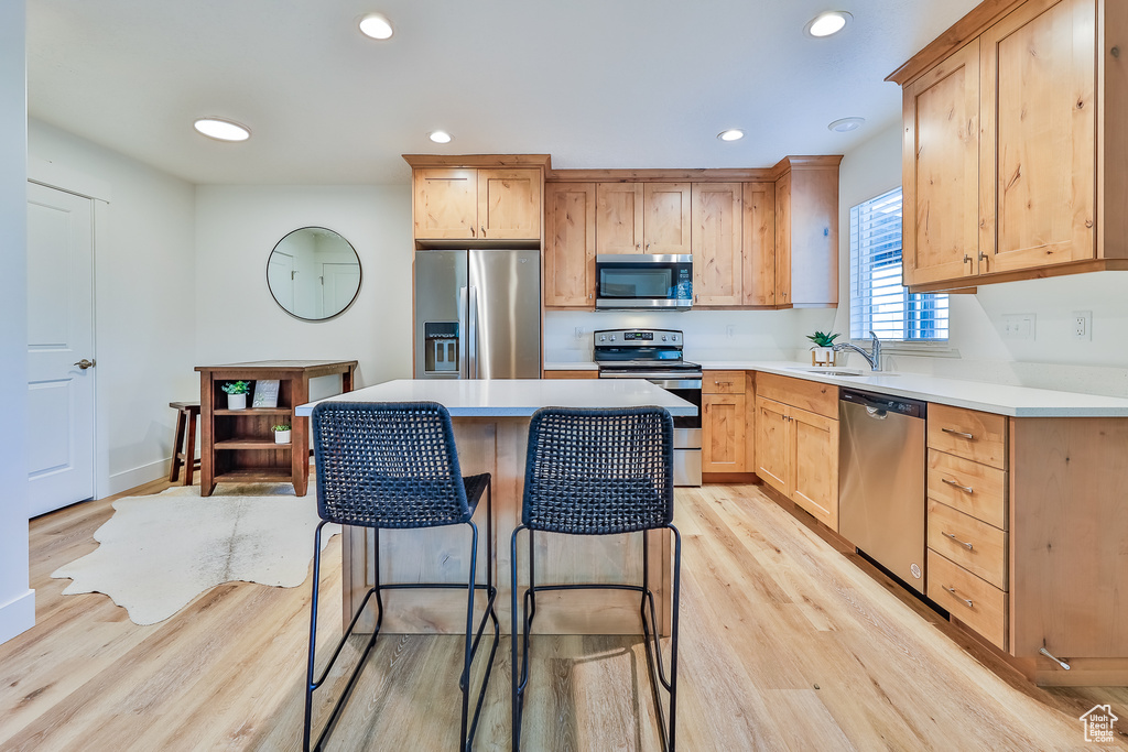 Kitchen featuring light hardwood / wood-style floors, appliances with stainless steel finishes, a kitchen island, and a breakfast bar