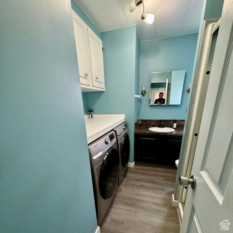 Laundry room featuring cabinets, light hardwood / wood-style floors, separate washer and dryer, and a textured ceiling