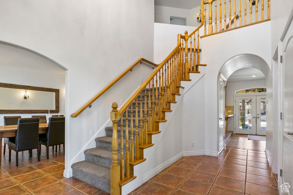 Staircase with french doors, a towering ceiling, and tile floors