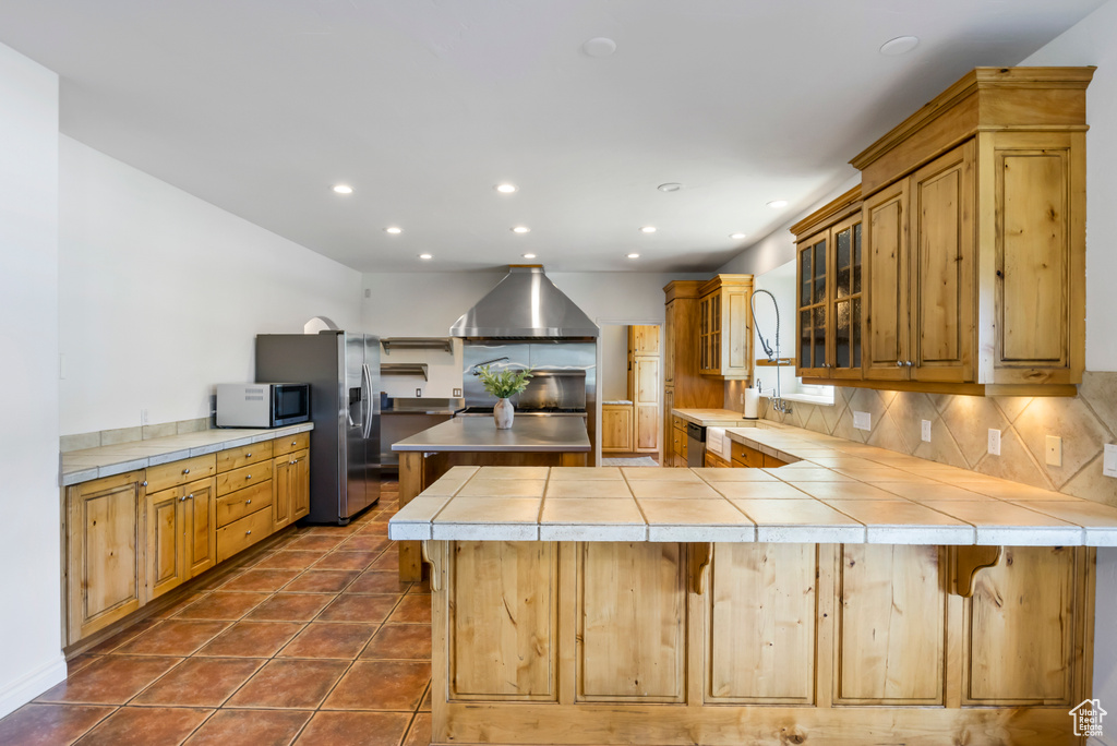 Kitchen featuring appliances with stainless steel finishes, dark tile flooring, tasteful backsplash, kitchen peninsula, and a kitchen breakfast bar