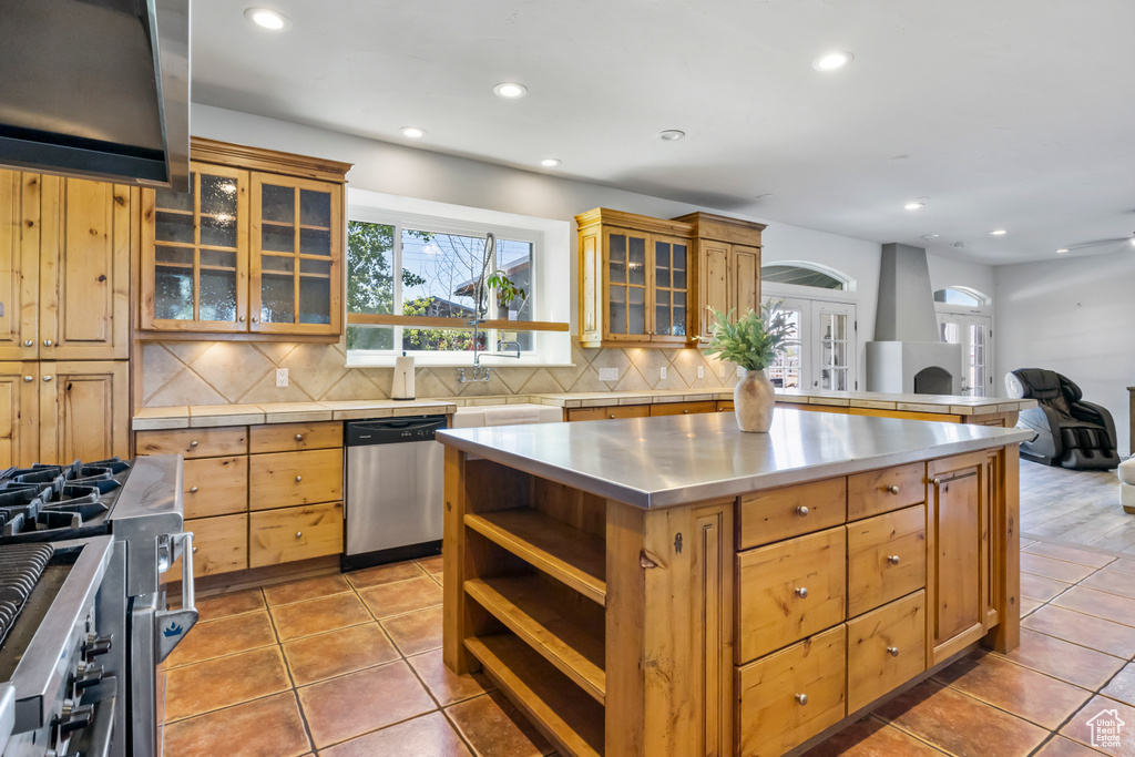 Kitchen featuring a center island, stainless steel counters, appliances with stainless steel finishes, light tile floors, and tasteful backsplash