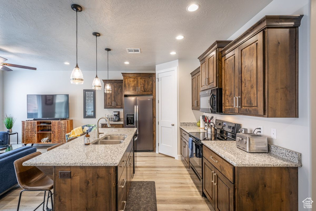 Kitchen featuring hanging light fixtures, light hardwood / wood-style floors, sink, black appliances, and ceiling fan