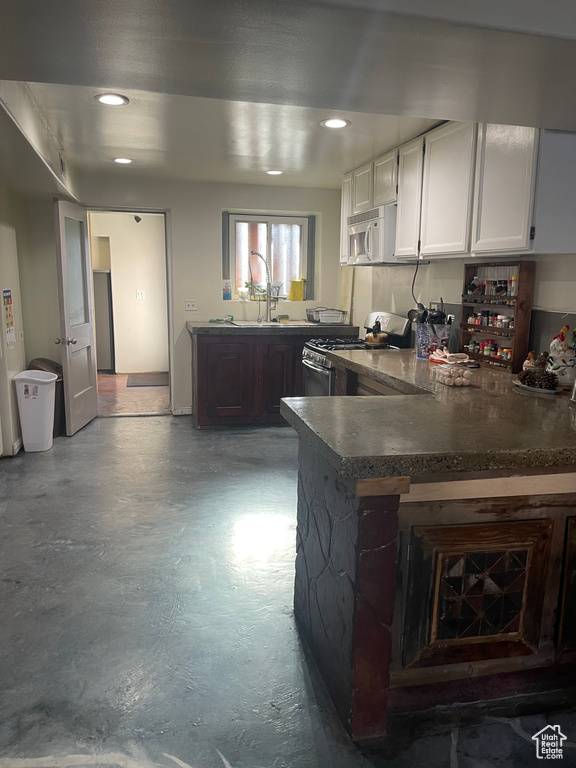 Kitchen with white cabinets, dark brown cabinets, sink, gas range, and kitchen peninsula