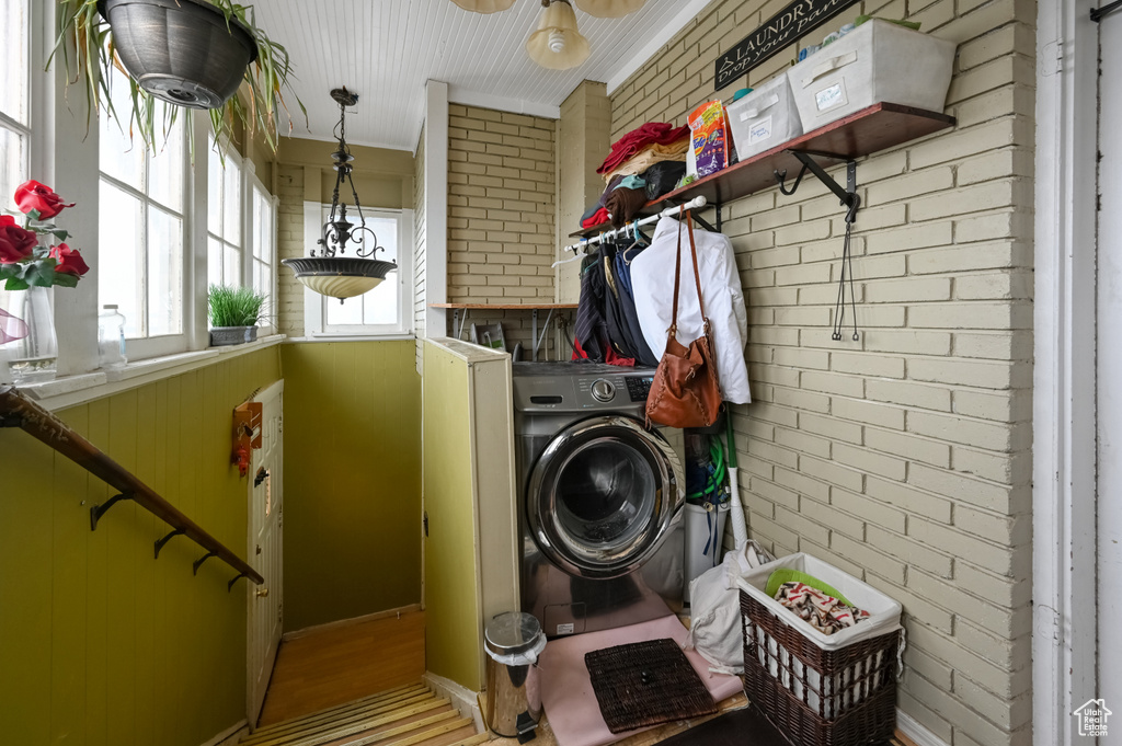 Clothes washing area featuring washer / clothes dryer, ornamental molding, brick wall, wood-type flooring, and ceiling fan