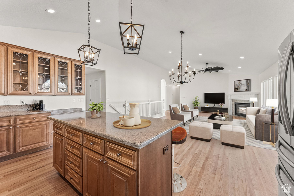 Kitchen with a kitchen island, light hardwood / wood-style floors, ceiling fan with notable chandelier, and lofted ceiling
