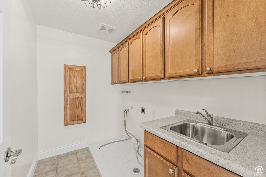 Laundry room featuring electric dryer hookup, a textured ceiling, sink, light tile floors, and cabinets