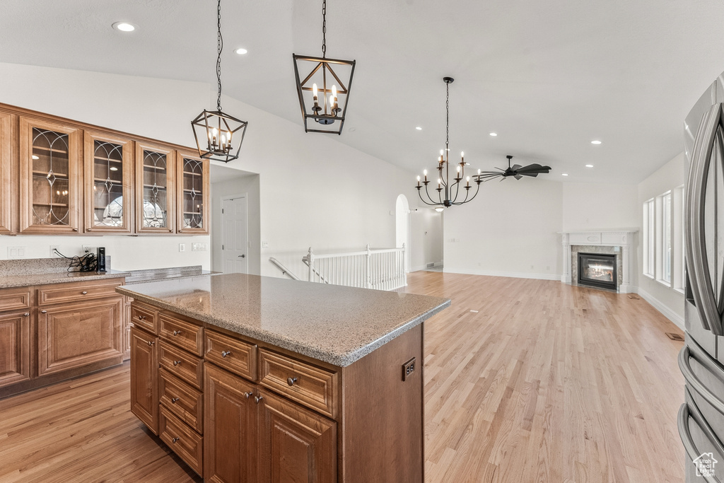 Kitchen featuring light wood-type flooring, pendant lighting, ceiling fan with notable chandelier, lofted ceiling, and a premium fireplace