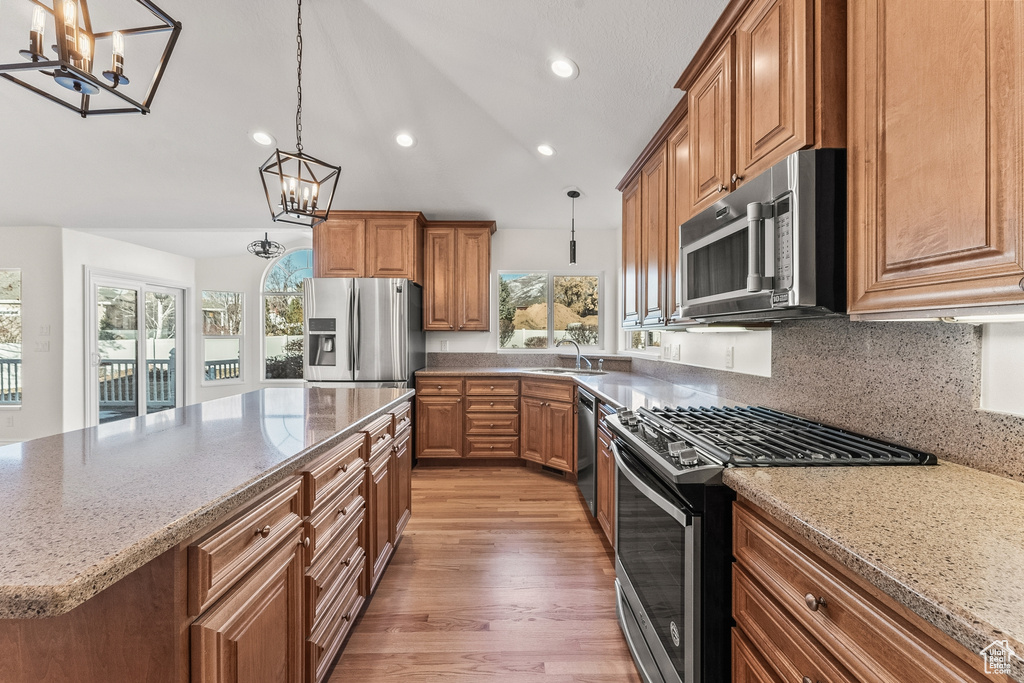 Kitchen with a kitchen island, light wood-type flooring, hanging light fixtures, an inviting chandelier, and appliances with stainless steel finishes