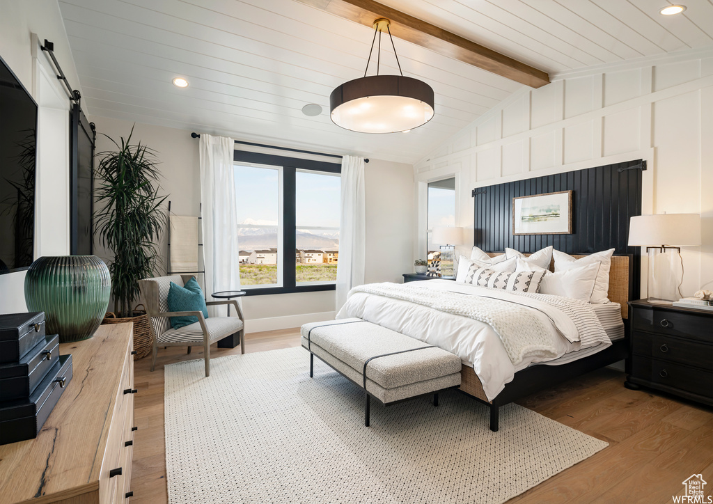 Bedroom featuring lofted ceiling with beams, a barn door, and light hardwood / wood-style floors