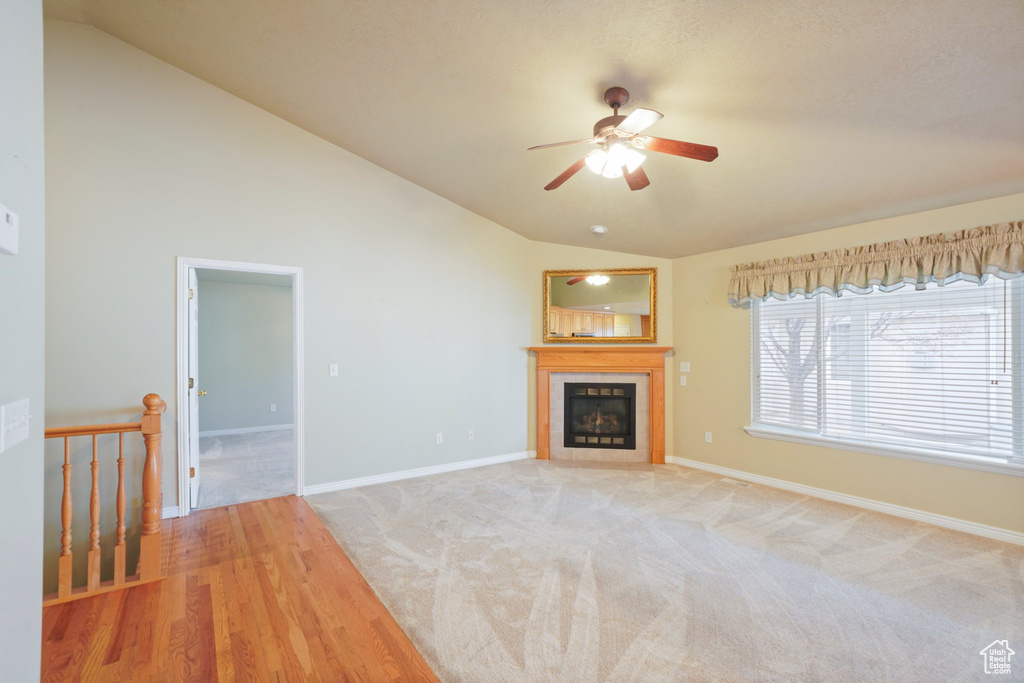 Unfurnished living room with a tiled fireplace, light hardwood / wood-style floors, vaulted ceiling, and ceiling fan