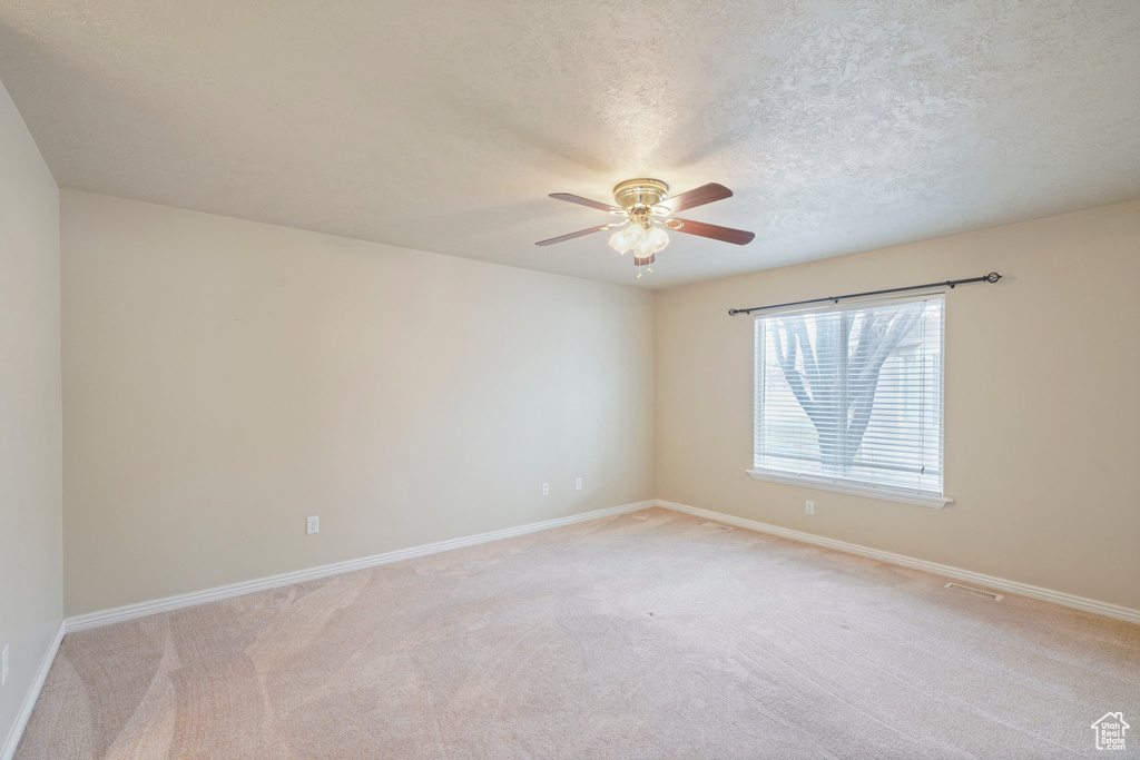 Empty room with ceiling fan, light colored carpet, and a textured ceiling