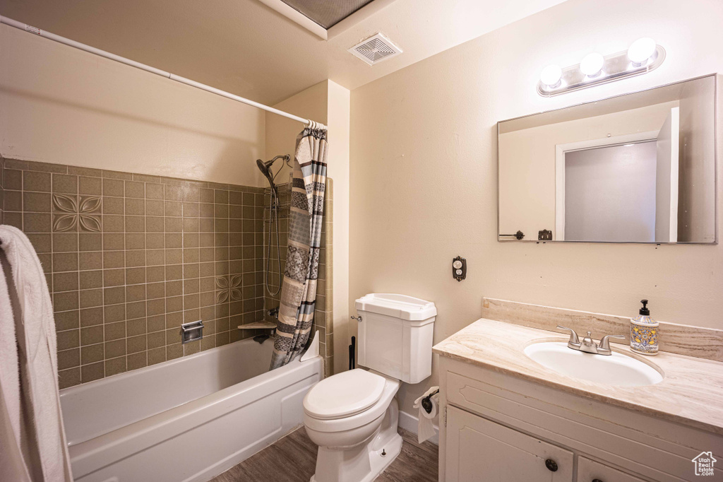 Full bathroom with hardwood / wood-style floors, toilet, shower / bath combination with curtain, and vanity with extensive cabinet space