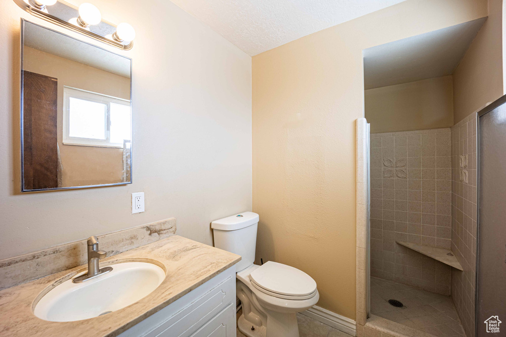 Bathroom featuring vanity, a textured ceiling, toilet, tile floors, and a tile shower