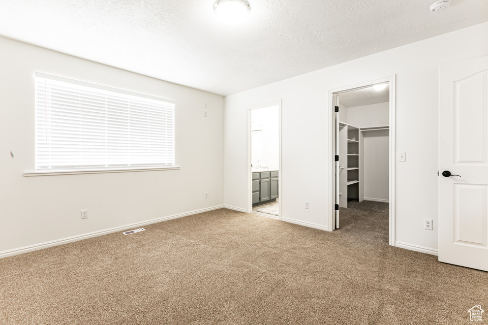 Unfurnished bedroom featuring connected bathroom, a walk in closet, a closet, and light colored carpet