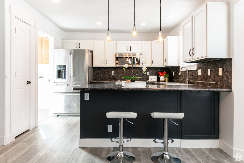 Kitchen with white cabinets, light hardwood / wood-style flooring, stainless steel appliances, and tasteful backsplash