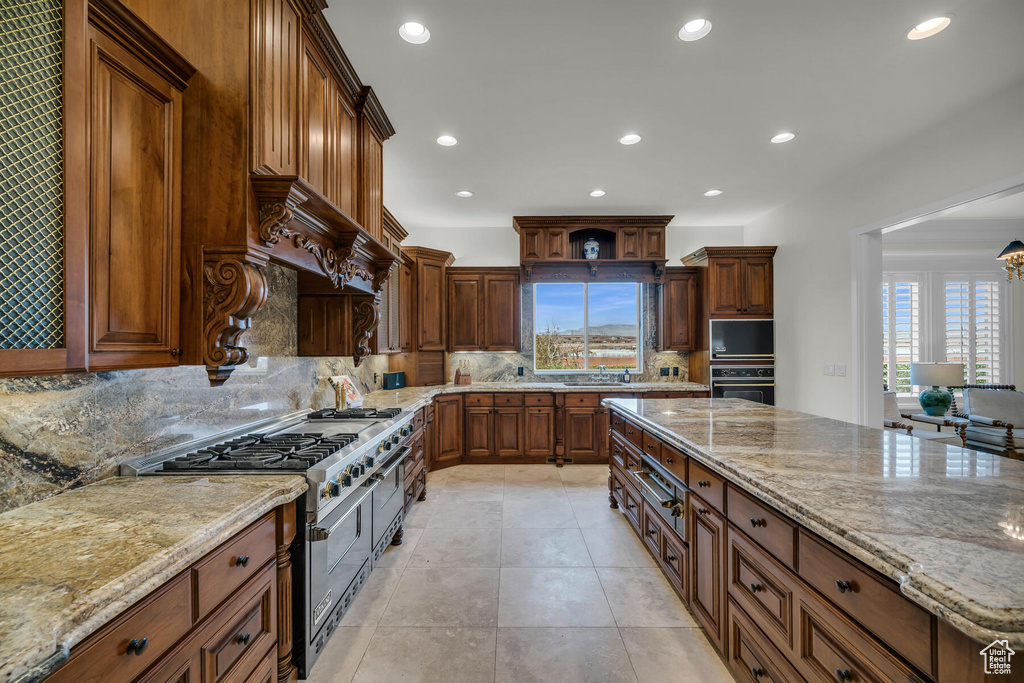 Kitchen with light stone counters, black appliances, tasteful backsplash, sink, and light tile floors