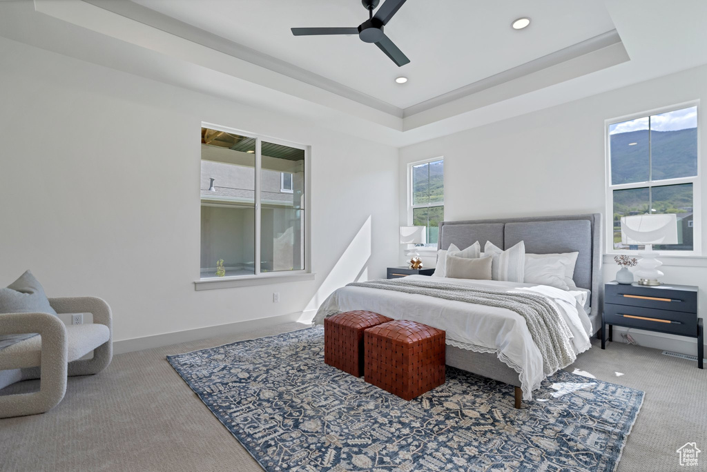 Bedroom with a raised ceiling, ceiling fan, multiple windows, and carpet flooring