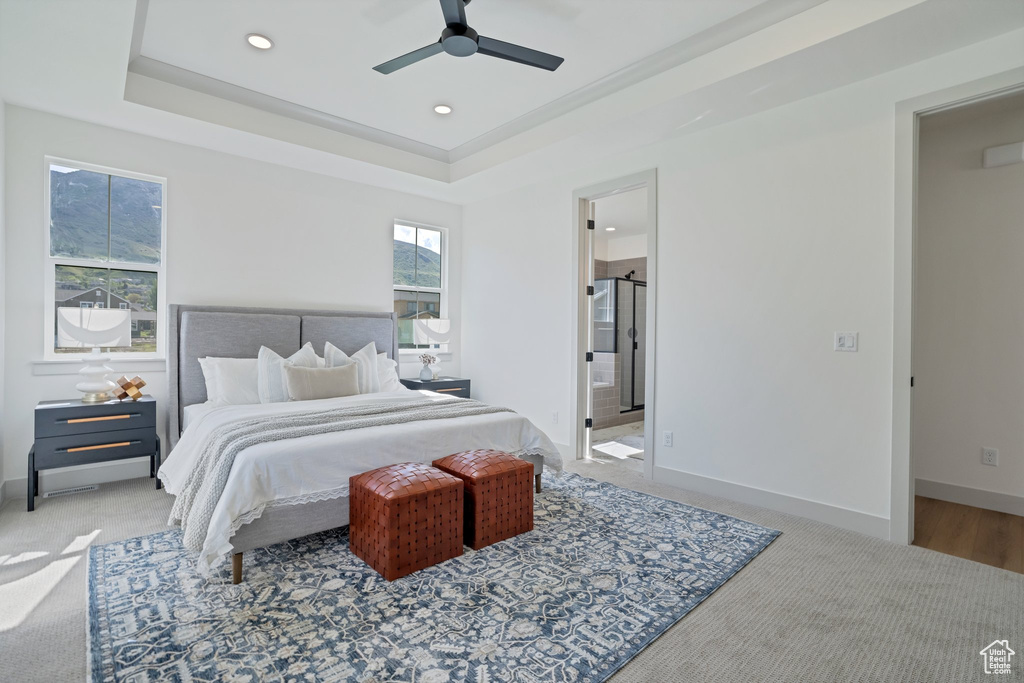 Bedroom with a raised ceiling, ceiling fan, ensuite bathroom, and carpet floors