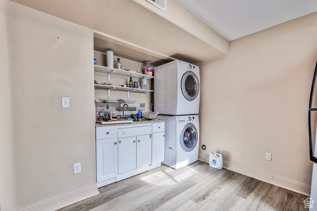 Laundry area featuring light hardwood / wood-style floors, sink, and stacked washer and clothes dryer