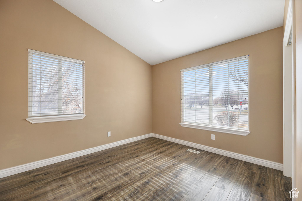 Empty room with vaulted ceiling and dark hardwood / wood-style flooring