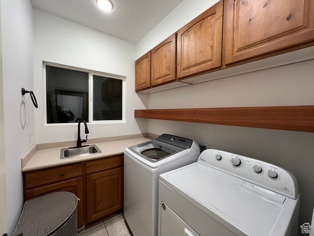 Washroom with light tile flooring, independent washer and dryer, cabinets, and sink
