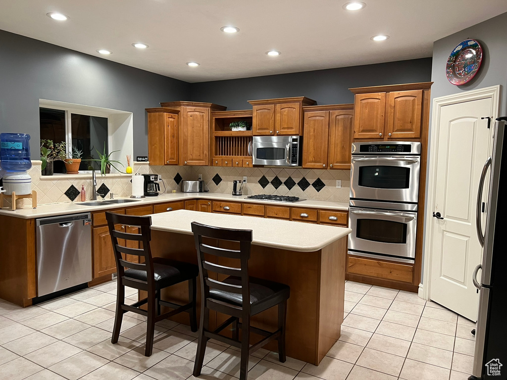 Kitchen with a kitchen island, backsplash, a kitchen bar, light tile flooring, and appliances with stainless steel finishes