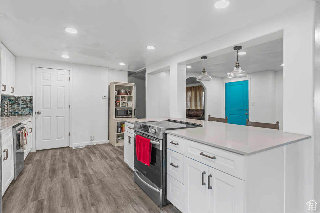 Kitchen with white cabinets, light hardwood / wood-style floors, stainless steel appliances, and decorative light fixtures