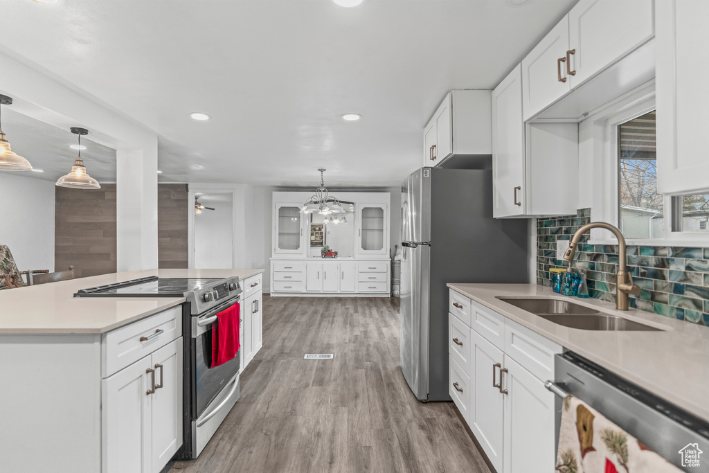 Kitchen with appliances with stainless steel finishes, hardwood / wood-style flooring, decorative light fixtures, and white cabinetry