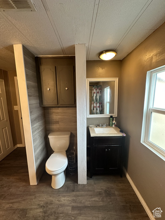 Bathroom featuring a textured ceiling, vanity, wood-type flooring, toilet, and wooden walls