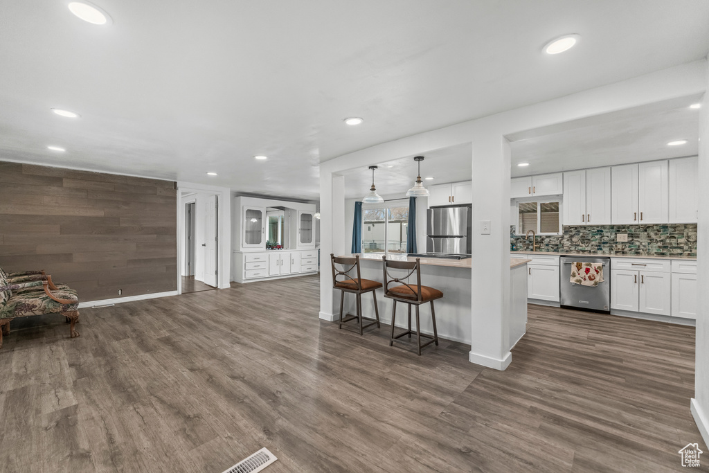 Kitchen featuring a breakfast bar area, white cabinetry, dark hardwood / wood-style flooring, decorative light fixtures, and appliances with stainless steel finishes