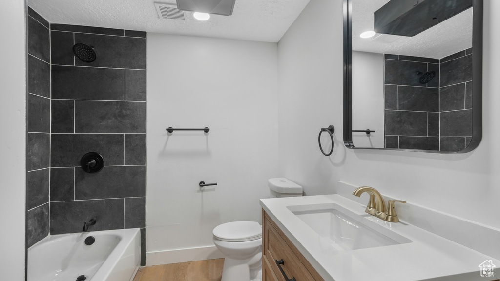 Full bathroom featuring a textured ceiling, tiled shower / bath combo, vanity with extensive cabinet space, hardwood / wood-style flooring, and toilet