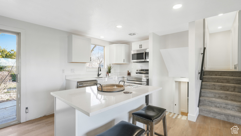 Kitchen featuring white cabinets, appliances with stainless steel finishes, light hardwood / wood-style floors, a kitchen breakfast bar, and a center island