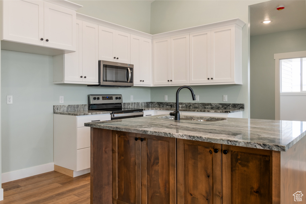 Kitchen featuring light wood-type flooring, white cabinets, dark stone countertops, appliances with stainless steel finishes, and sink