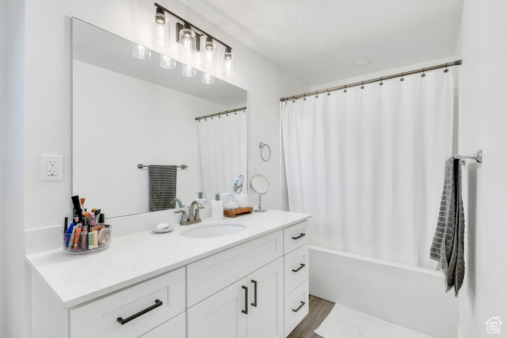 Bathroom featuring hardwood / wood-style floors, shower / bathtub combination with curtain, oversized vanity, and a textured ceiling
