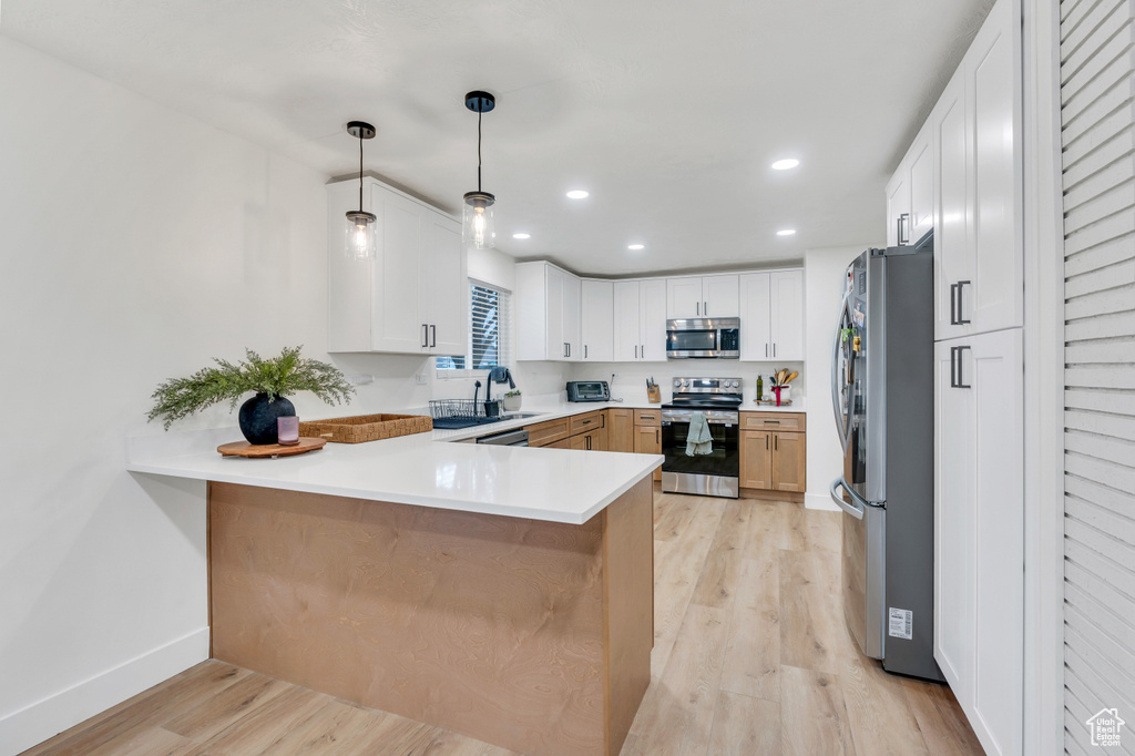 Kitchen featuring light hardwood / wood-style floors, white cabinets, hanging light fixtures, kitchen peninsula, and appliances with stainless steel finishes