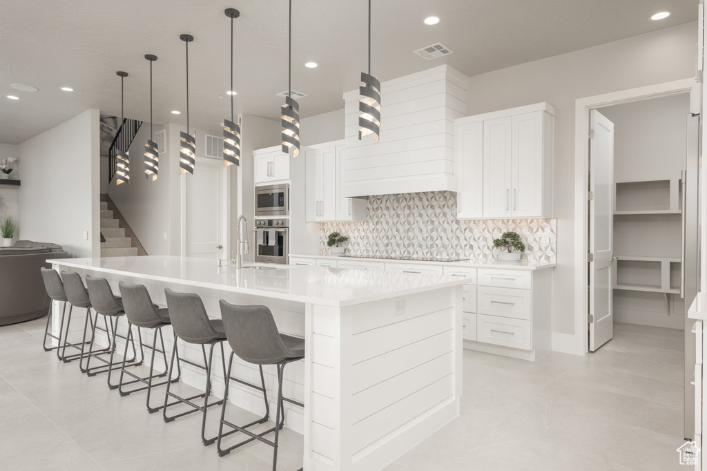 Kitchen with appliances with stainless steel finishes, an island with sink, tasteful backsplash, and white cabinets