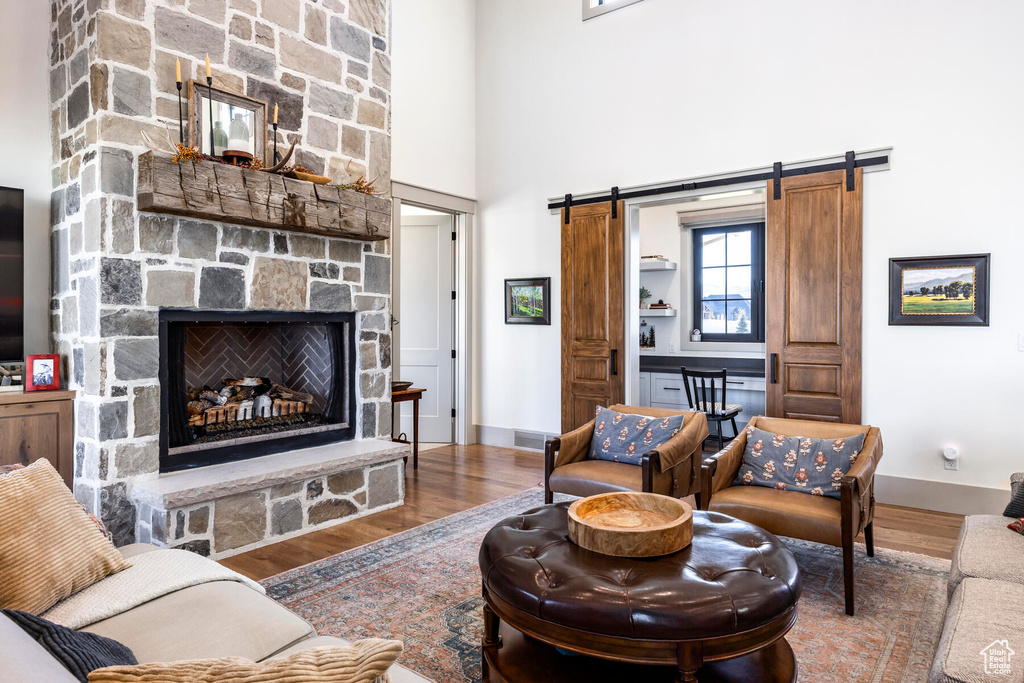 Living room featuring a barn door, dark wood-type flooring, a towering ceiling, and a stone fireplace