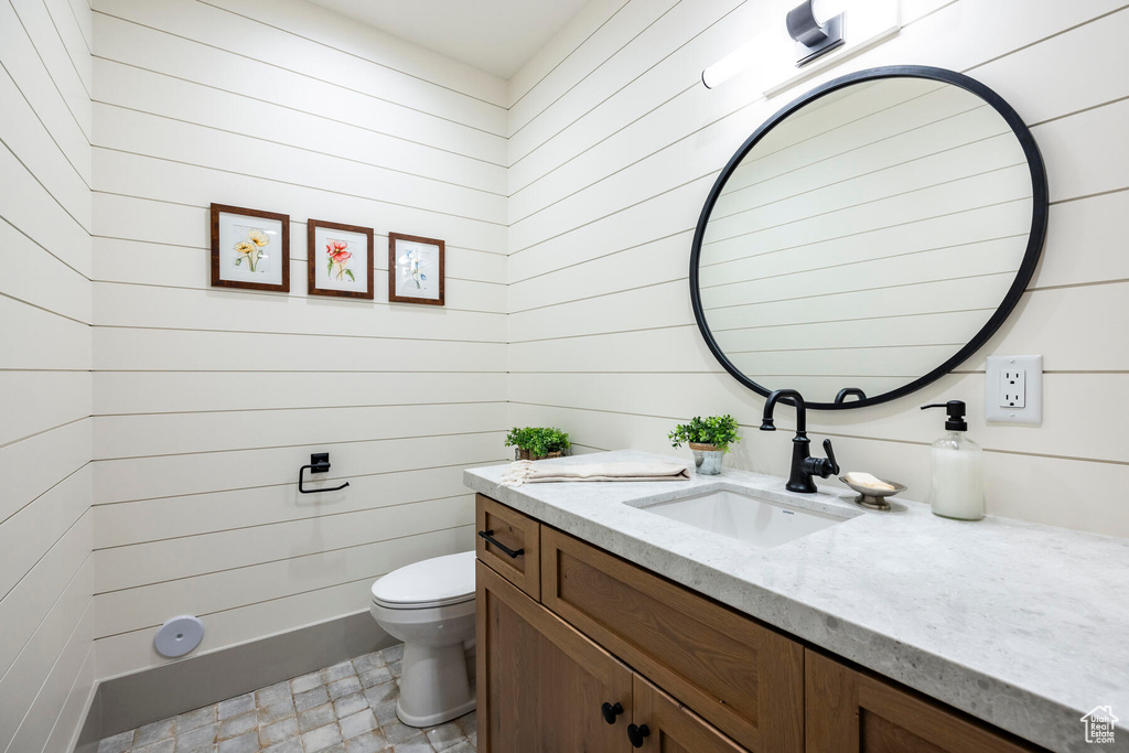 Bathroom with toilet, wooden walls, large vanity, and tile floors