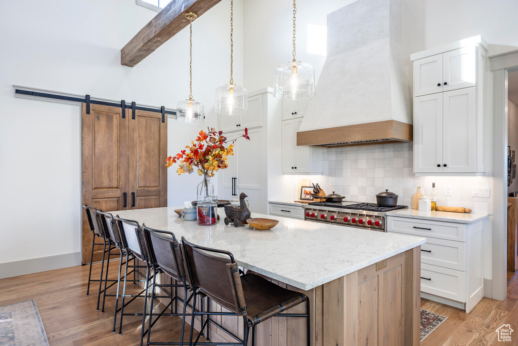 Kitchen featuring custom exhaust hood, light wood-type flooring, white cabinets, tasteful backsplash, and a barn door