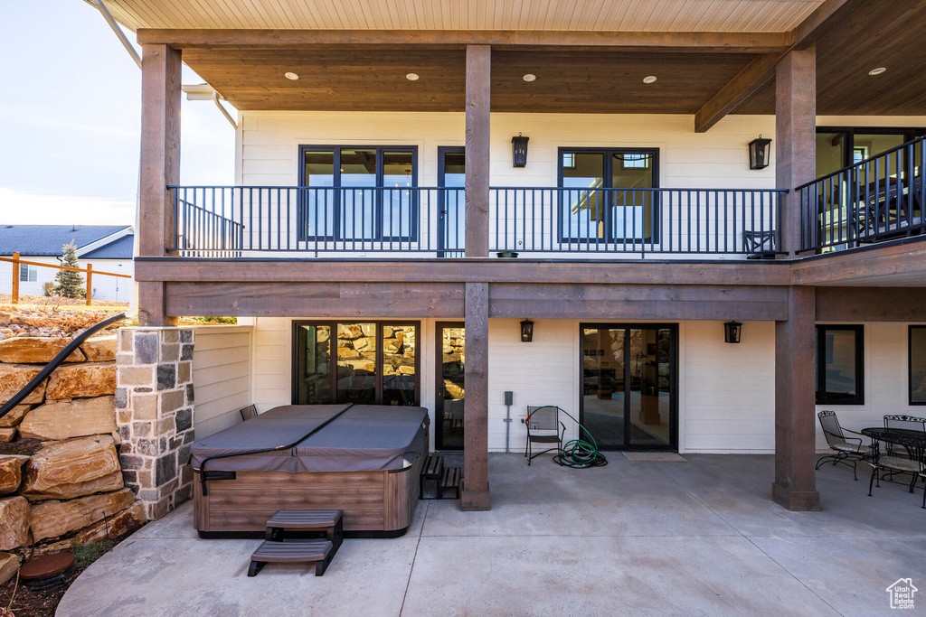 Back of property with a balcony, a hot tub, and a patio