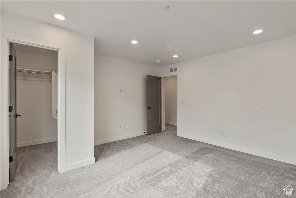 Unfurnished bedroom with a walk in closet, a closet, and light carpet
