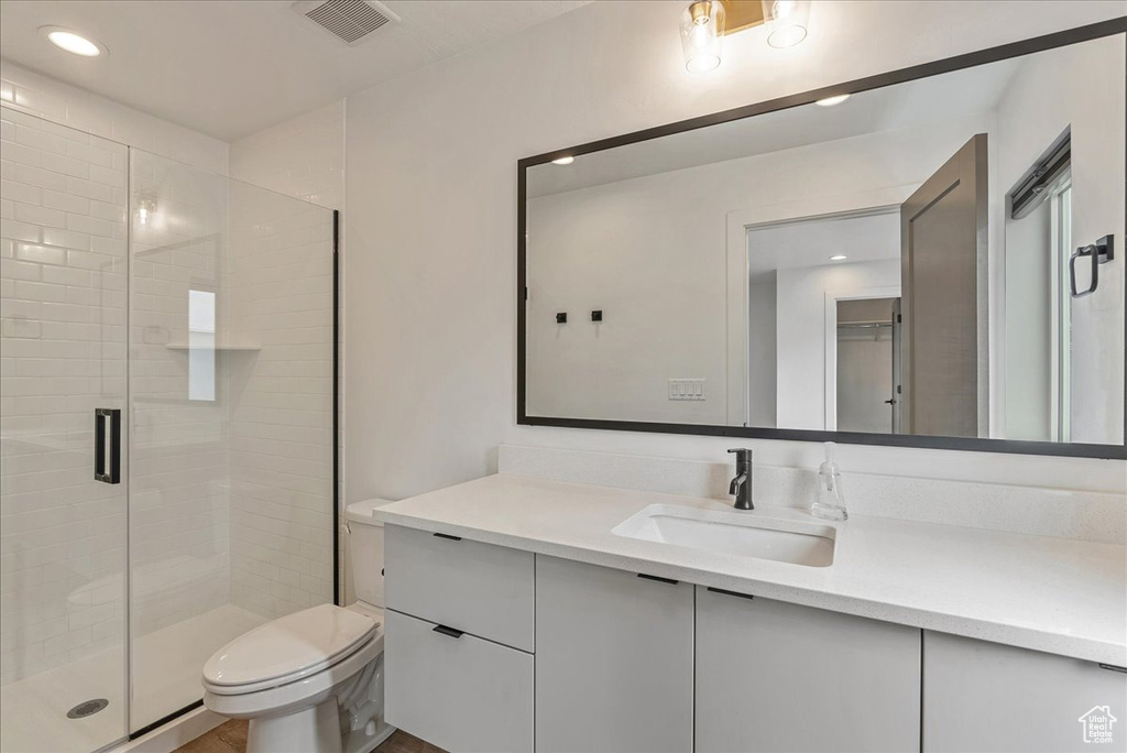 Bathroom featuring toilet, a shower with door, and vanity with extensive cabinet space